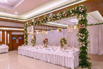 Elegant Wedding Reception Stage Decor with Floral Arrangements and Seating. Elegant Wedding Hall with White Chairs and Stage Decorations. Elegant Wedding Reception Table with Floral Decorations
