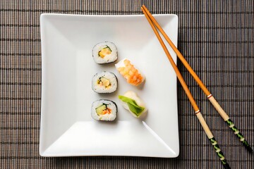 Fresh sushi rolls on a white plate with chopsticks on a bamboo mat background