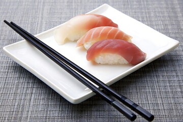 Fresh sushi selection with various fish on a white plate with black chopsticks on a gray background