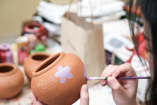 Cheerful young woman painting ceramics in a pottery workshop Enjoying Art in Thailand, Selective focus. - Powered by Adobe