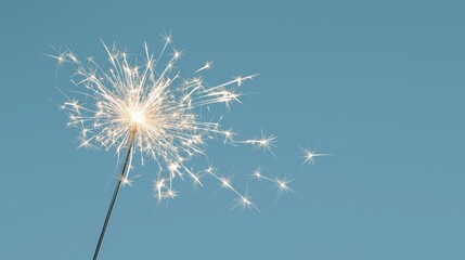 Naklejka premium Sparkler ignites with bright white sparks against a clear soft blue sky