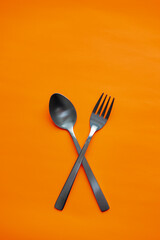 Black Spoon and Fork Crossed on Orange Background