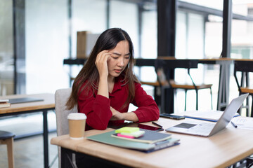 feeling stressed asian businesswoman working on laptop sitting at desk in modern office space for...