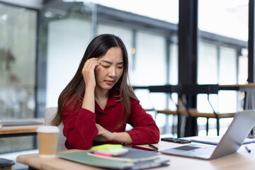 feeling stressed asian businesswoman working on laptop sitting at desk in modern office space for...
