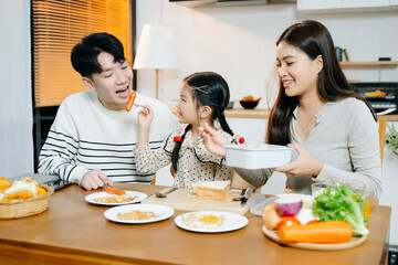 Asian family shares a happy morning, preparing and enjoying breakfast in a cozy kitchen. Parents...