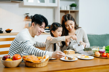 Asian family shares a happy morning, preparing and enjoying breakfast in a cozy kitchen. Parents...