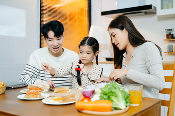 Happy Asian parents and daughter enjoying healthy breakfast together at home. Candid lifestyle...