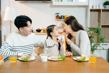 Asian father reads book to daughter at breakfast while mom prepares food. Heartwarming family...