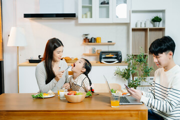 Asian father reads book to daughter at breakfast while mom prepares food. Heartwarming family...