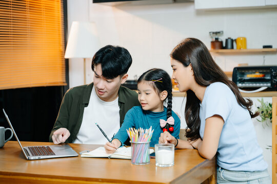 Asian parents support their daughter with schoolwork at home. Family bonding over learning, reading, and education in a cozy modern kitchen with warm lighting