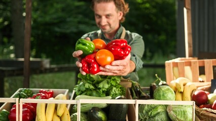 Handsome bearded worker selling fresh products at farmers market counter. Positive man holding vegetables and proposing to buy them. Joyful smiling and looking at camera. Nutrition concept.