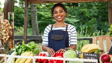 Cute African American female seller working at market. Positive woman selling organic natural...