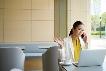 Businesswoman discussing work on the phone while using her laptop and drinking coffee
