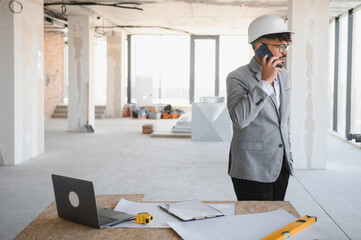 Arab Architect wearing hardhat talking on phone at construction site