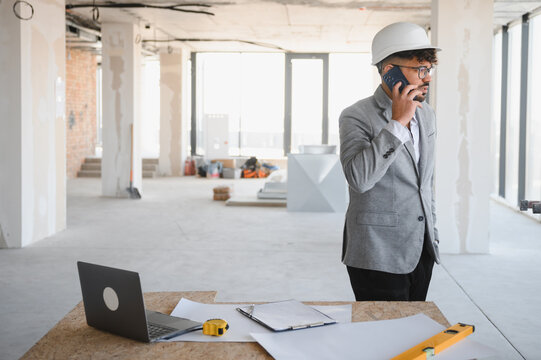 Arab Architect wearing hardhat talking on phone at construction site
