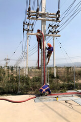 Vertical shot of the electricians working on the electric post power pole for the power cable installation.