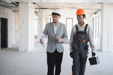 Architect showing blueprint to builder during construction inspection