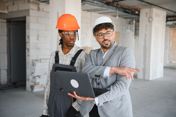 Architect showing construction plan on laptop to builder in building under construction