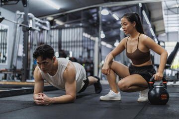 Personal trainer watching client doing plank exercise in gym