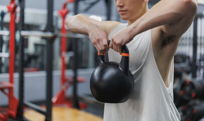 Determined asian athlete lifting kettlebell in modern gym for fitness training