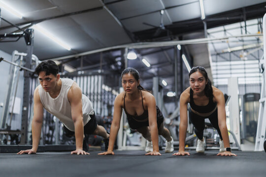 Determined asian athletes performing push ups in modern gym - Powered by Adobe