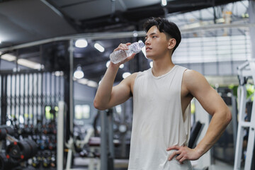 Young athlete drinking water after intense workout in gym