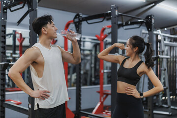 Young couple drinking and showing muscles in gym