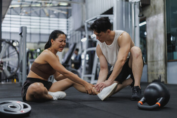 Asian sportswoman suffering ankle injury at gym with personal trainer assisting
