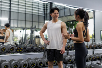 Personal trainer supporting client choosing correct dumbbells in gym