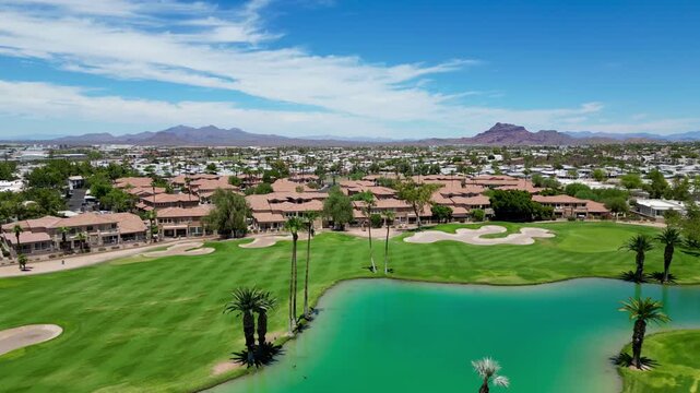 Aerial view of a green golf course with palm trees, lake, and homes under a clear blue sky