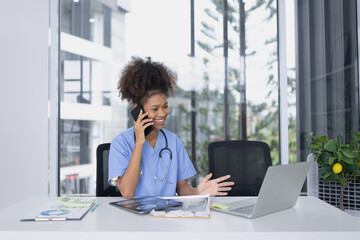 African American female doctor using mobile phone with laptop working at clinic office, Medical and health care concept.