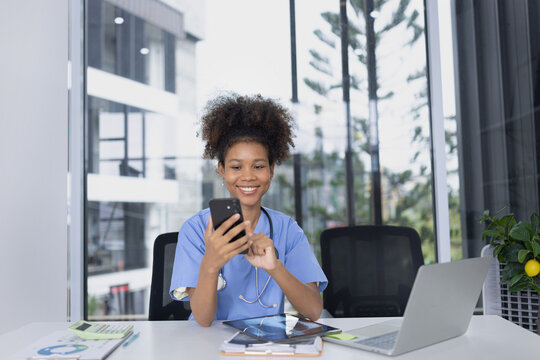 African American female doctor using mobile phone with laptop working at clinic office, Medical and health care concept. - Powered by Adobe