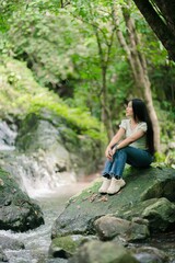 Serene Female Model Sitting by Waterfall Surrounded by Lush Greenery