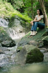 A Young Woman Relaxing by a Serene Waterfall in Lush Green Nature