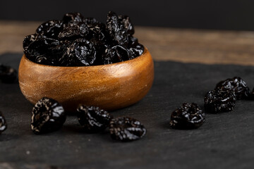 old bowl filled with dried prunes close up, dark-colored dried plum fruits poured into a bowl