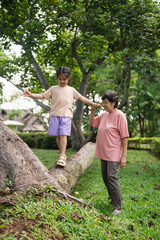 Joyful moments of a child balancing on a tree branch with caring grandmother watching in a serene garden setting filled with lush greenery