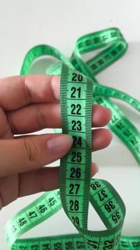 A two-meter green ribbon in a woman's hand on a white background. The concept of diet, weight loss. Ribbon for sewing.