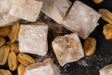 Turkish delight scattered on the table, sugar cubes with starch and toasted peanuts on a black...
