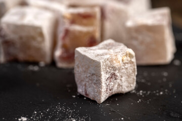 sweet lukum slices with cherry slices on a black board , cubes of sweet Turkish delight with the addition of dried red berries in powdered sugar