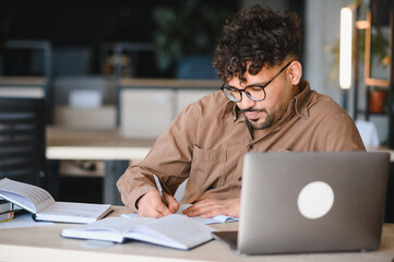 Focused arab student studying and taking notes in university library