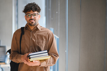 Smiling arab student holding books in university hallway