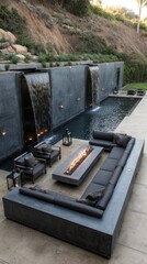 Modern patio with fire pit, water features, and comfortable seating.  Large, dark gray sectional sofa, fire pit, and waterfalls are featured.  Outdoor living space