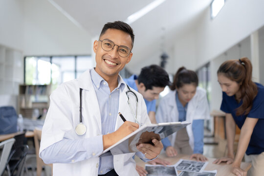 A male doctor smiling looking at the camera in meeting room, Medical team reviewing data. - Powered by Adobe