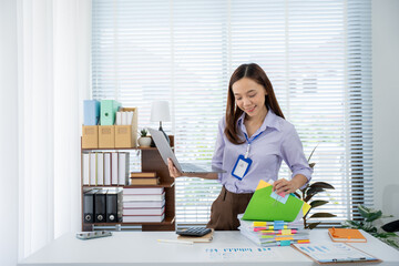 Working in Office: A diligent woman, engrossed in paperwork and a laptop, is hard at work in a...