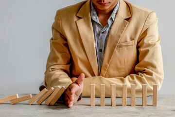 Man In Tan Suit Halts Domino Fall Mid-Sequence, Symbolizing Crisis Prevention And Control