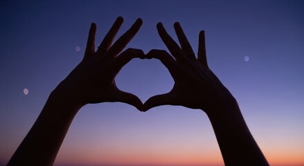 Silhouette of hands forming a heart shape against a colorful sunset sky with soft light and dark shadows