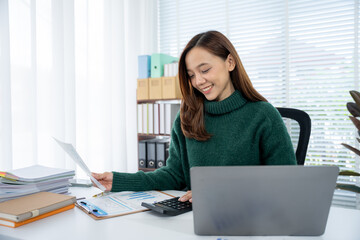 Office Productivity: A young woman is engrossed in her work at a sunlit office desk, analyzing...