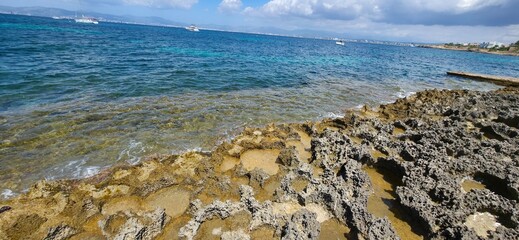 Jagged limestone rocks and shallow turquoise water stretch toward the horizon under a partly cloudy...