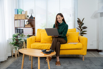 Working from Home Bliss: A woman, immersed in her work on a laptop, radiates content comfort while perched upon a vibrant yellow sofa, a harmonious blend of productivity and serene leisure.
