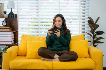 Gamer's Joy on the Sofa: A young woman engrossed in mobile gaming sits cross-legged on a vibrant...